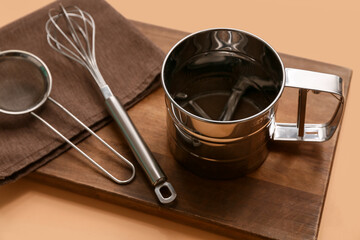 Metal sieves, whisk, napkin and wooden board on color background