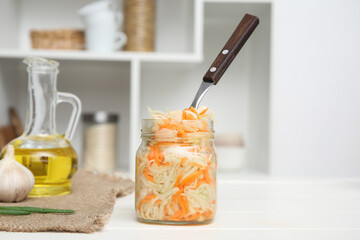 Jar with sauerkraut and fork on table in kitchen. Closeup