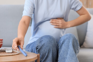 Young pregnant woman with gestational diabetes taking lancet pen from table at home, closeup