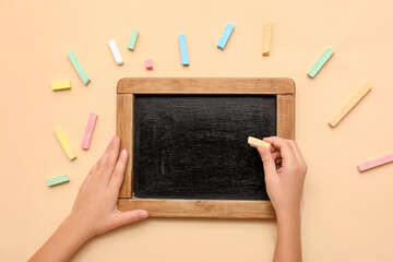 Child's hands drawing on blackboard with chalk on beige background. Top view