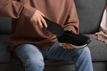 Young man putting black orthopedic insole into sneaker at home, closeup