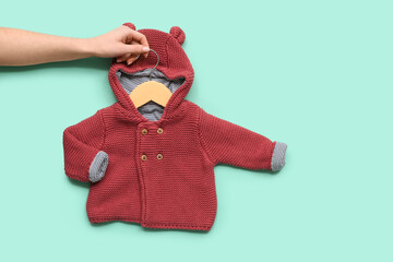 Female hand with stylish baby sweater on color background