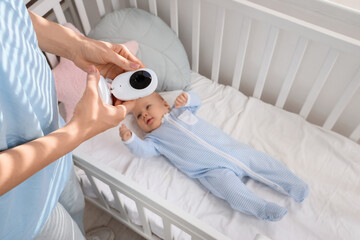 Mother holding baby monitor near her child in crib, closeup