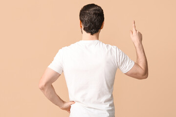Young man pointing up on beige background, back view