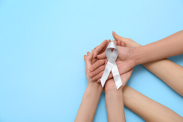 Female hands with grey awareness ribbon on blue background. Brain cancer concept
