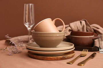 Stack of clean dishes with golden cutlery and gypsophila flowers on brown background