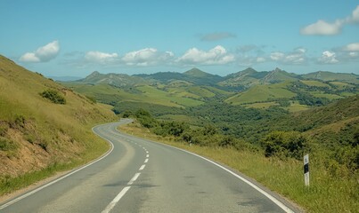 Naklejka premium Asphalt Road Winding Through Verdant Valley Under Blue Sky