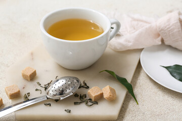 Cup of hot green tea with sugar cubes, strainer and dried leaves on white background