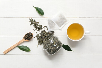 Cup of hot green tea and jar with dried leaves on white wooden background