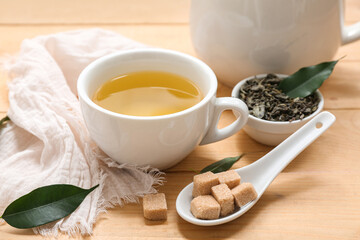 Cup of hot green tea with sugar cubes and dried leaves on wooden background, closeup