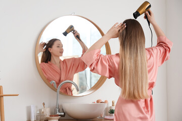 Young woman using hair dryer in bathroom