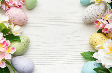 Colorful easter eggs and spring flowers creating a frame on white wood