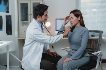 Obraz premium Young practitioner using stethoscope examining lungs of female patient suffering headache during medical consultation in hospital office or clinic