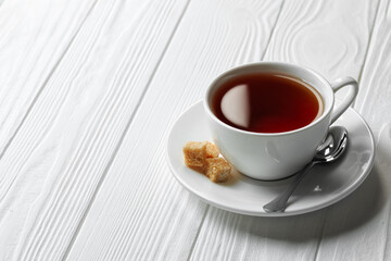 black tea in cup on saucer with spoon and sugar cubes on white wooden table
