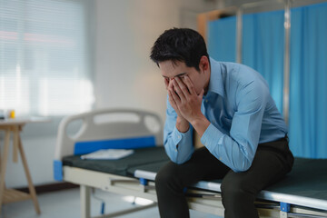Young businessman sitting on a hospital bed, covering his face with his hands, feeling overwhelmed by stress and anxiety related to health and business challenges