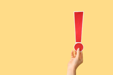 Female hand with red paper exclamation mark on color background