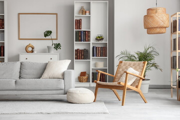 Bookcase, cozy sofa and wicker armchair in interior of stylish living room