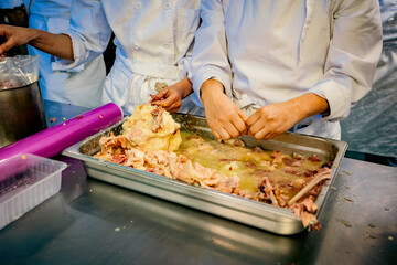 Group of chefs in white uniforms preparing and processing raw meat in a professional kitchen. Hands-on culinary training focused on food preparation and hygiene standards.