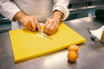 Close-up of a chef finely chopping ingredients on a yellow cutting board in a professional kitchen. Precision knife skills are key to culinary expertise and food preparation.