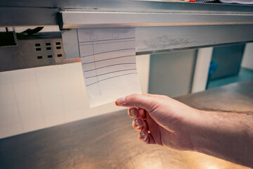 Chef reviewing order tickets in a busy restaurant kitchen. Waiter waits for plated dish. Coordination, teamwork, and efficiency in food service.