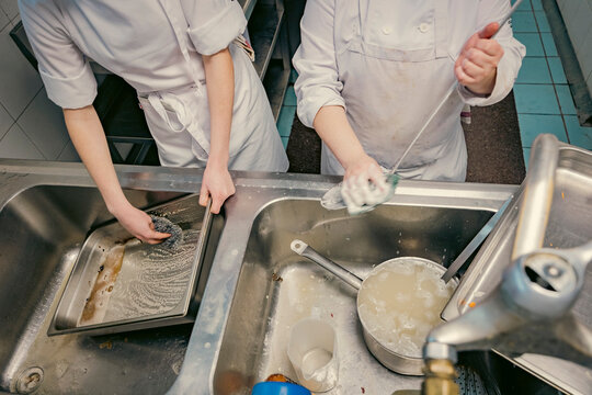 Chefs scrubbing and cleaning dishes in a busy professional kitchen. Hygiene, teamwork, and kitchen maintenance are essential in the food industry.