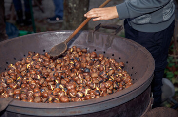 Roasting chestnuts in a large pan outdoors with wooden spoon