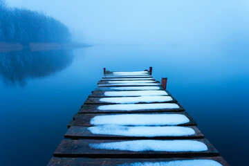 Obraz premium Snow on the jetty and a calm misty lake