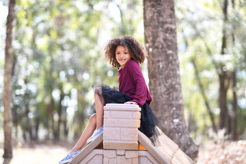 Smiling girl sitting atop a playhouse roof, enjoying an outdoor