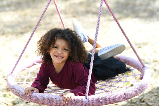 Smiling girl lounging on a pink rope swing, enjoying outdoor pla