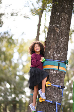 Smiling girl climbing a tree using colorful handholds outdoors