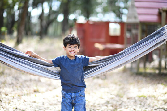 Smiling boy standing in a hammock, playfully stretching his arms