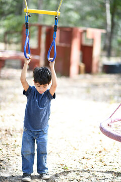 Young boy gripping playground rings, hanging with determination