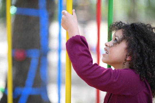 Smiling girl gripping colorful playground bars, looking up excit