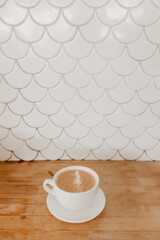 Latte with leaf latte art in white cup on wooden table and tiled wall