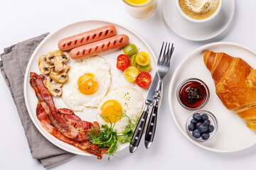 A classic breakfast plate featuring sunny-side-up eggs, crispy bacon, sausages, and fresh tomatoes