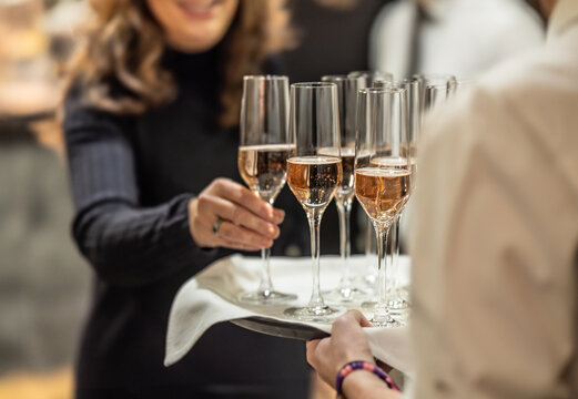 Young waiter holding a tray with champagne or prosecco at a wedding or gala event and offering guests a welcome drink