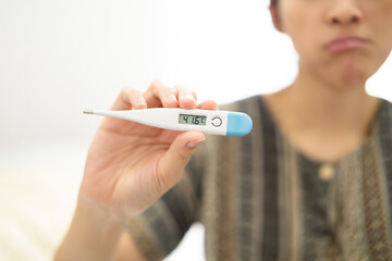 Digital thermometer showing high temperature held by person expressing discomfort, representative...