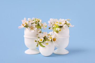 White eggs in white stands with spring pear and strawberry flowers on a blue background. Happy Easter
