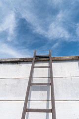 Weathered ladder leads to bright sky over a white wall on a sunny day