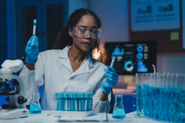 Young female scientist wearing lab coat and gloves comparing two test tubes with blue liquid in a...