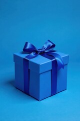 Obraz premium A single, square gift box, adorned with a vibrant blue ribbon and bow, rests on a matching blue background.