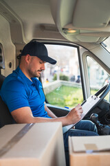 Delivery driver in van recording deliveries with clipboard. Delivery driver concept in a van. Man...
