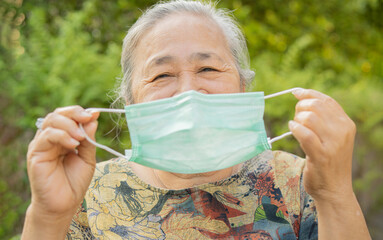Close-up portrait of happy senior woman holding medical mask outdoors. Looking at camera.
