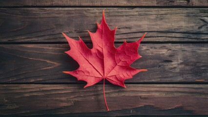 Obraz premium Vibrant red maple leaf prominently centered on rustic wooden surface with deep brown and gray tones highlighting natural textures and details