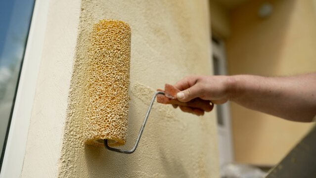 House painter carefully applying paint on exterior facade using small roller during home renovation and maintenance work