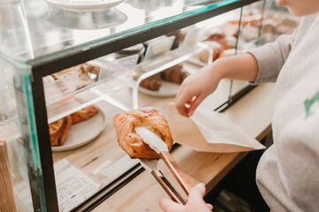 Barista using tongs to place a pastry into a bag at cafe counter