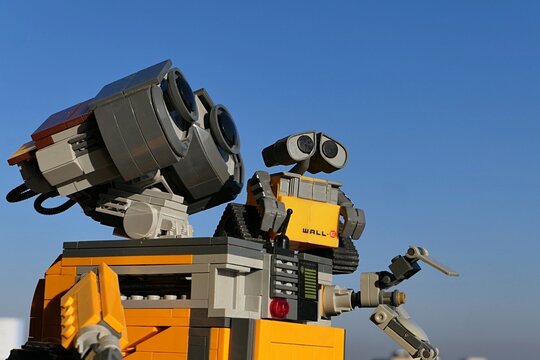LEGO Wall-E robot model from Disney Pixar science fiction movie  of the same name, with smaller Wall-E model sittin on his chassis, looking forward. Blue skies in background. 