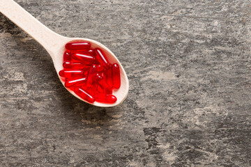 Vitamin capsules in a spoon on a colored background. Pills served as a healthy meal. Red soft gel...