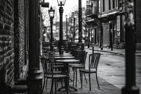 Fototapeta A black and white photograph of an empty outdoor café with vintage street lamps, evoking a sense of quiet urban solitude on a serene city street corner.