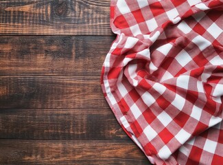 Obraz premium A red and white checkered tablecloth on a rustic wooden background, perfect for a cozy picnic or dining setting.